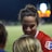 A female athlete in a red sports jersey with the NWSL logo energetically interacts with others on a sports field. The backdrop consists of a darkened night sky and a blurred scoreboard or advertisement display, with soft, colorful lights.
